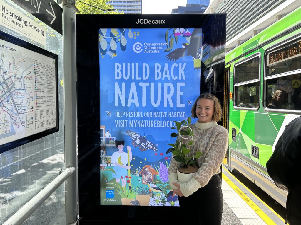 Lizzie from Bupa stands in front of a Nature Blocks™ tram stop advertisement.